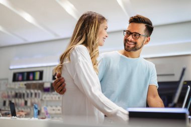 Genç ve tatmin olmuş bir çift, teknoloji mağazasının masasındaki cep telefonunun yeni modelini test ediyor..