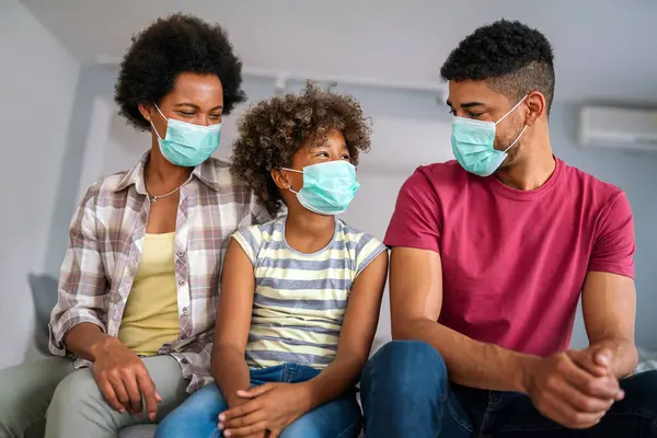 Young african american family in medical masks during home quarantine. Family is wearing facemasks during coronavirus and flu outbreak. Virus and illness protection, COVID