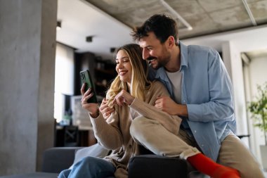 Akıllı telefona bakarken kucaklaşan gülümseyen genç çift. Sosyal medyayı akıllı telefondan paylaşan çok ırklı çift.