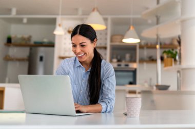 Evde bilgisayarla çalışan mutlu genç bir kadın. Çevrimiçi öğrenim gören çekici iş kadını, dizüstü bilgisayar, web sörfü bilgileri veya internet mağazasından alışveriş yapıyor..