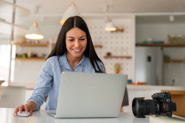Evde dizüstü bilgisayarla çalışan bir kadın. Serbest fotoğrafçı bilgisayardaki fotoğrafları düzenliyor. Profesyonel fotoğraf işi. Bilgisayar ve fotoğraf makineli kız çalışma alanı. Yaratıcı sanatçı yaşam tarzı