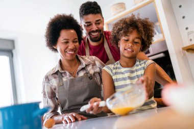 Coşkulu Afro-Amerikalı çocuklu genç bir aile evde birlikte yemek pişiriyor, mutlu gülümseyen ebeveynler hafta sonları mutfakta çocukla eğleniyor.