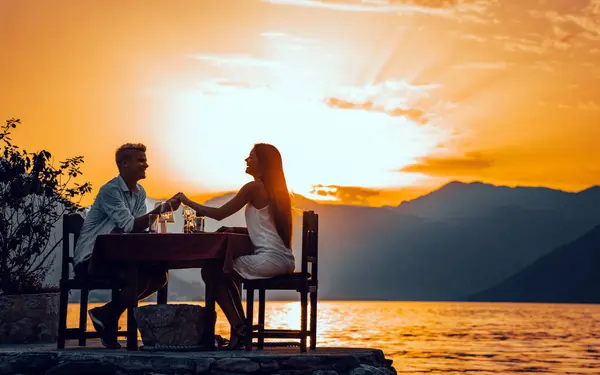 Couple in love drinking champagne wine on romantic dinner at sunset on the beach. Young couple celebration anniversary, clink glasses at served table on sea
