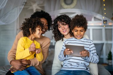 Mutlu çoklu etnik aile dijital cihazlarla eğleniyor. Homoseksüel ebeveynler ve küçük çocuklar dijital tablet kullanıyorlar..