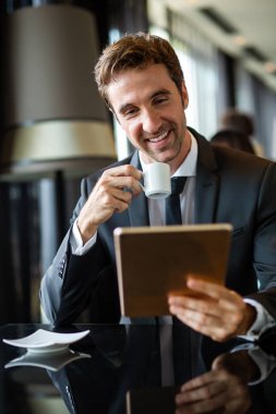 Genç, modern, başarılı iş adamı ofiste otururken dijital tablet kullanıyor.