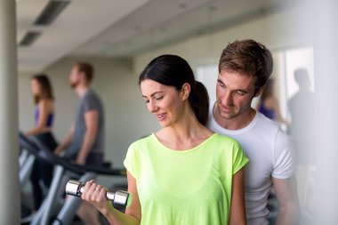 Yakışıklı erkek özel antrenörü spor salonunda halterlerle çalışan güzel bir kadına yardım ediyor.