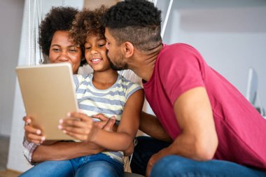 Mutlu Afro-Amerikan ailesi evde aletle eğleniyor. Siyah ebeveynler ve çocuklar dijital tablet kullanıyorlar