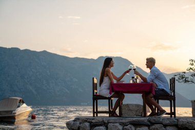 Aşık bir çift plajda gün batımında romantik bir akşam yemeğinde şarap içiyor. Genç çift yıldönümü, balayı, doğum günü.