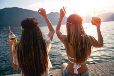 Mutlu kızlar yaz tatilinde sahilde kokteyl içerek eğleniyorlar. İnsanlar eğlence konseptiyle seyahat eder