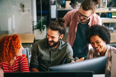 Mixed team of software engineers brainstorming ideas for new code library in front of computer screens compiling algorithms. Diverse app developers collaborating on group project in it agency office.