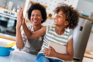 Eğitim, aile çevrimiçi öğrenme kavramı. Tablet bilgisayarlı Afrika kökenli anne ve kız evde ödev yapıyorlar.