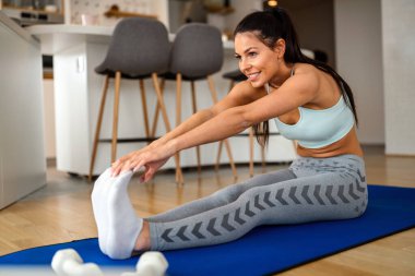 Genç bir kadın egzersiz yapıyor, evde egzersiz yapıyor, oturma odasında sağlıklı kalmak için antrenman yapıyor. Spor insanları konsepti.