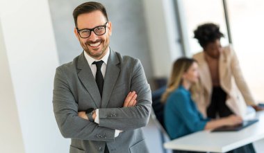 Genç, mutlu, genç ve başarılı bir iş adamı kollarını kavuşturup şirkete gülümsüyor.