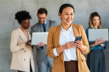 Arka planda çok ırklı meslektaşlar çalışırken başarılı iş kadını ve girişimcinin portresi.