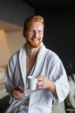 Yakışıklı, kaslı, genç bir adam sabah kahvesini otel odasında içiyor. İnsanlar hafta sonu seyahat eder..