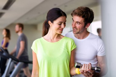 Yakışıklı erkek özel antrenörü spor salonunda halterlerle çalışan güzel bir kadına yardım ediyor.