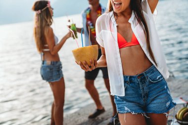 Plaj partisinde tropikal kokteyllerle eğlenen mutlu genç arkadaşlar. Seyahat ve yaz tatili konsepti.