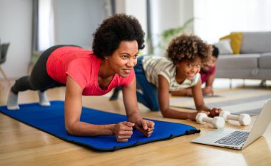 Mutlu genç anne ve kız yoga yapıyor, evde birlikte, spor minderinde oturuyor, sağlıklı yaşam tarzının tadını çıkarıyorlar.