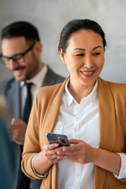 Ofisteki Orta yaşlı Asyalı iş kadını. Başarılı bir kadın cep telefonuyla mesaj atıyor ve çalışıyor. Gülümseyen iş kadını.