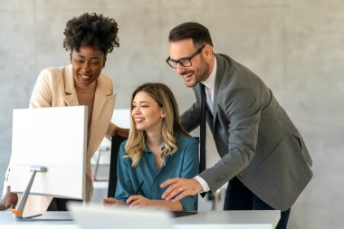 Çeşitli etnik çeşitlilikte mutlu iş adamları ofiste bilgisayarın etrafında toplandı