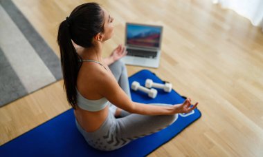 Evde spor yapmak, internetten video izlemek, dizüstü bilgisayarla çalışmak. Sağlıklı kalmak için spor yapan mutlu zinde bir kadın..