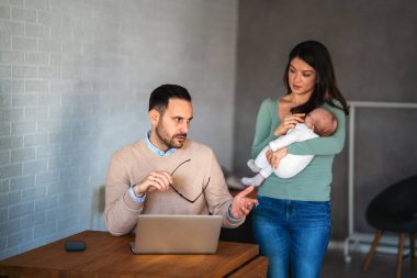 Baba işadamı, evde karısı ve bebeği varken dizüstü bilgisayarla çalışmaya çalışıyor. Aşırı çalışma, aile sorunları stres konsepti.