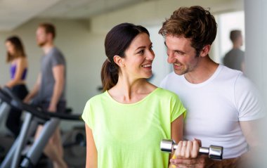 Yakışıklı erkek özel antrenörü spor salonunda halterlerle çalışan güzel bir kadına yardım ediyor.