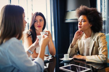 Kadın ve müşterileri iş görüşlerini tartışıyor ve bir kafede kahve içerken işbirliği yapıyorlar. Mutlu iş ortakları bir öğle yemeği toplantısında birbirleriyle iletişim kurarken dijital bir cihaz kullanıyorlar..