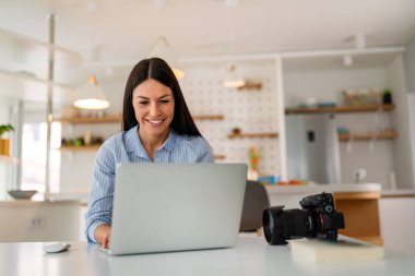 Evde dizüstü bilgisayarla çalışan bir kadın. Serbest fotoğrafçı bilgisayardaki fotoğrafları düzenliyor. Profesyonel fotoğraf işi. Bilgisayar ve fotoğraf makineli kız çalışma alanı. Yaratıcı sanatçı yaşam tarzı