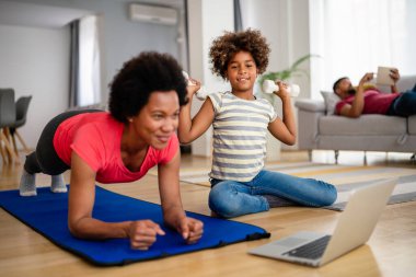 Çocuklu mutlu, Afro-Amerikalı bir kadın çevrimiçi video sporları eğitimi izliyor ve spor paspası üzerinde esniyor. Evde aile kavramı, sağlık, spor ve yoga