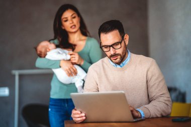 Baba işadamı, evde karısı ve bebeği varken dizüstü bilgisayarla çalışmaya çalışıyor. Aşırı çalışma, aile sorunları stres konsepti.