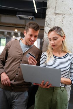 Evde kredi kartı ve bilgisayarla alışveriş yapan gülümseyen genç bir çift. Bilgisayarı kullanarak ecommerce sitesinden alırken bankamatik kartı tutan mutlu çift..