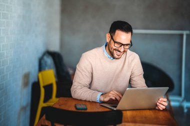 Teknoloji, uzak iş ve yaşam tarzı konsepti. Bilgisayarlı başarılı genç adam ev ofisinde çalışıyor.