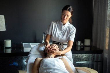 Yüz masajı. Güzellik salonunda masaj yaptıran genç bir kadının yakın çekimi. Kaplıca ve vücut bakımı. Yüz güzelliği tedavisi. Kozmetoloji.