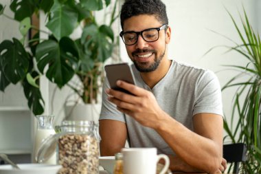 Mutlu Afro-Amerikan adam kahvaltı yaparken cep telefonu kullanıyor. İnsanlar teknoloji aleti konsepti