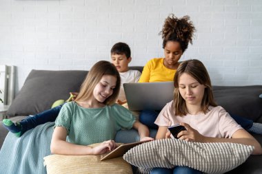 Modern aletleri ve dizüstü bilgisayarı olan bir grup genç evde birlikte ders çalışıp eğleniyorlar.