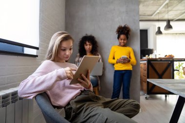 Modern aletleri ve dizüstü bilgisayarı olan bir grup genç evde birlikte ders çalışıp eğleniyorlar.