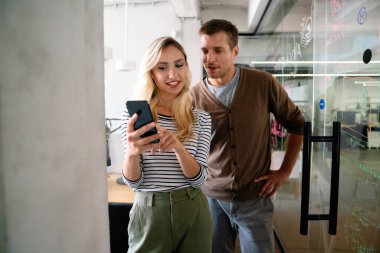 Erkek bir iş arkadaşıyla tartışıyor, akıllı bir telefona bakıyor ve ofiste birlikte çalışıyor.