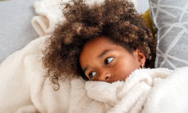 Dalgın üzgün Afro-Afrikalı Amerikalı çocuk, evde yastığa uzanmış bir kız. Hasta çocuk virüs çocuk konsepti