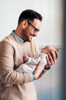 Sevgi dolu baba yeni doğmuş bebeğini evde taşıyor. Mutlu bir babanın parlak portresi. Elinde uyuyan bebeği tutuyor..