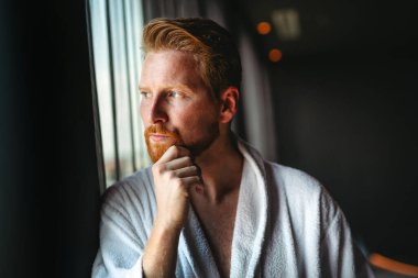 Depresyondaki genç adam evdeki pencereye bakıyor. Hayal kırıklığına uğramış erkek, kişisel hayat konseptinde mutsuz bir sorun hissediyor