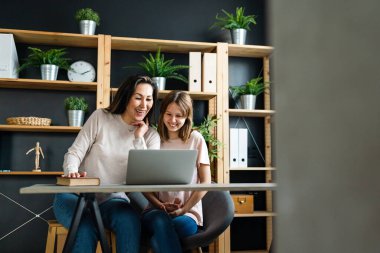 Mutlu genç Asyalı bekar anne evde eğitim görürken dizüstü bilgisayar kullanarak tatlı bir kızla ders çalışıyor.