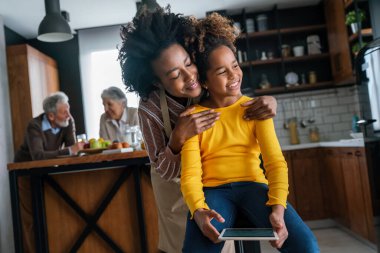 Eğitim, aile ve öğrenme kavramı. Tablet bilgisayarlı anne ve kızı evde ödev yapıyor.