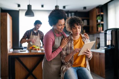 Eğitim, aile ve öğrenme kavramı. Tablet bilgisayarlı anne ve kızı evde ödev yapıyor.