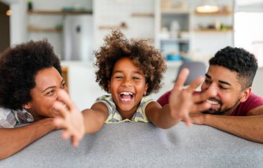 Happy biracial girl smiling with young multiracial parents enjoy weekend at home together, overjoyed multiethnic daughter play with loving mom and dad clipart