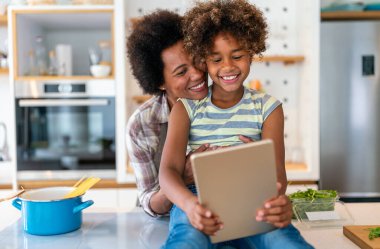 Eğitim, aile çevrimiçi öğrenme kavramı. Tablet bilgisayarlı Afrika kökenli anne ve kız evde ödev yapıyorlar.