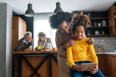 Eğitim, aile ve öğrenme kavramı. Tablet bilgisayarlı anne ve kızı evde ödev yapıyor.