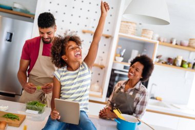 Happy african american smiling family preparing healthy food in kitchen, having fun together on weekend clipart