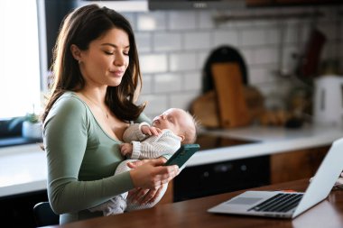 Evde kal anne. Bebeğine bakarken uzaktan bilgisayarla çalış. Annelik iznindeki genç anne çocuğuyla birlikte masa başında serbest çalışmaya çalışıyor.