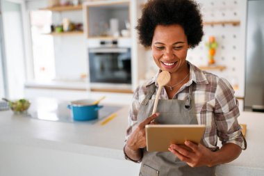 Genç Afrikalı Amerikalı kadın mutfağında yemek pişirmek için tablet bilgisayar kullanıyor. İnsanlar teknoloji gıda kavramı.